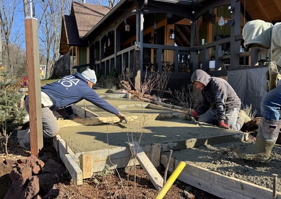 Workers screeding a poured slab beside a timber-framed building