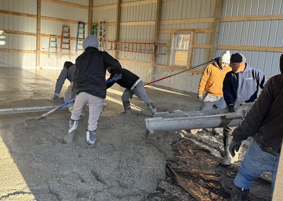 Workers smoothing a large interior concrete floor inside a steel building