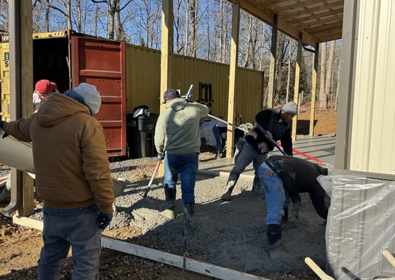 Crew pouring concrete beside a shipping container on a covered site