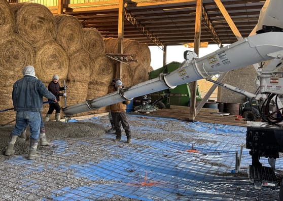Concrete being poured over reinforcing mesh in a barn interior